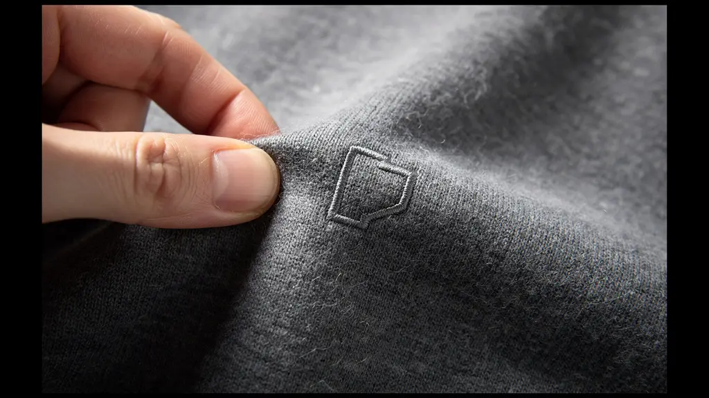 Gros plan sur la texture d'un sweat premium neutre, sans logo lisible, avec une main qui en montre la qualité.